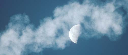 The exhaust trail of the Delta-II drifts across the half moon on December 7, 2001